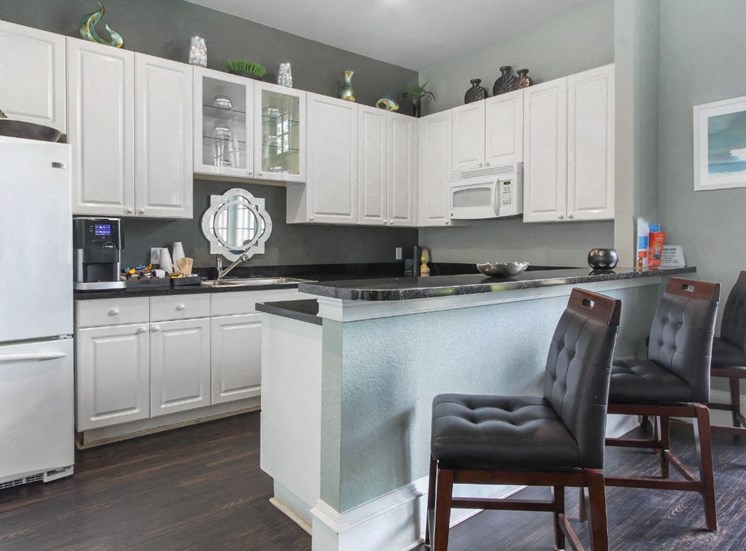 Decorated Clubhouse Kitchen with White Cabinets White Appliances with Black Counters and Brown Bar Stools